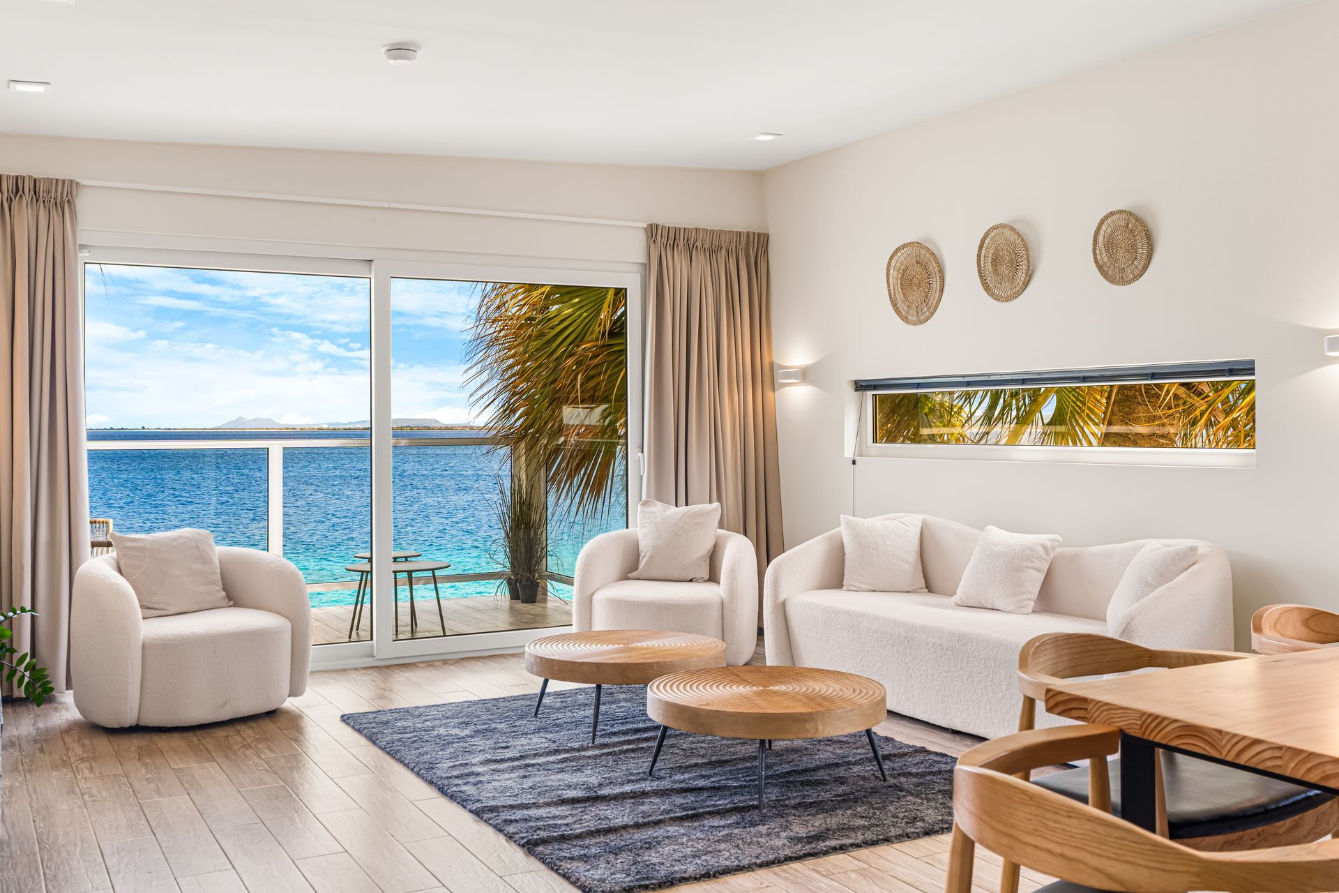 Bright seaside living room with white furniture, blue rug, and ocean view through large sliding doors