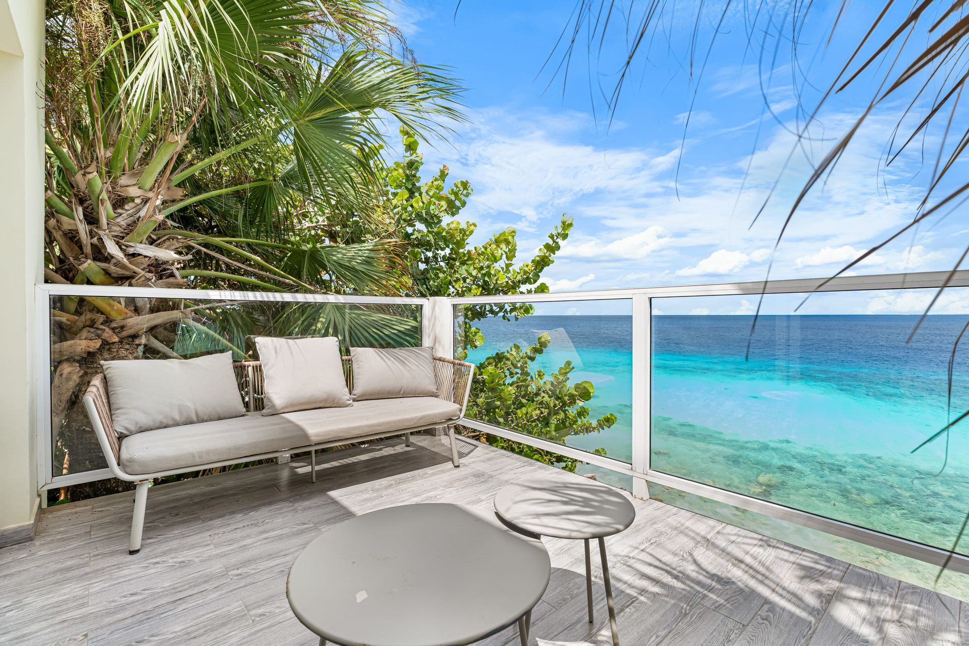 Oceanfront patio with beige lounge sofa, glass railing, and turquoise sea view