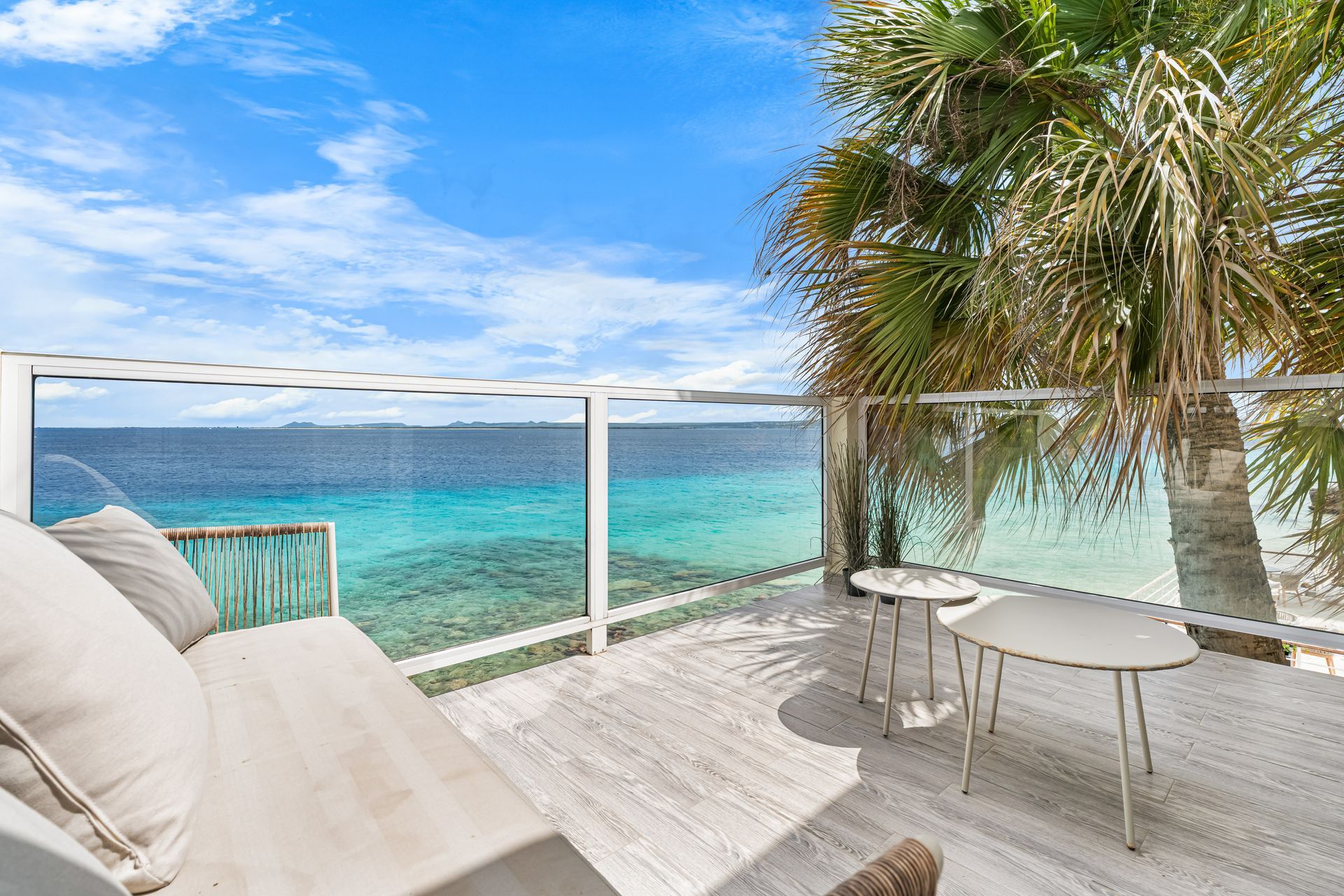 Oceanfront balcony with white lounge chairs, table, and turquoise sea under a blue sky
