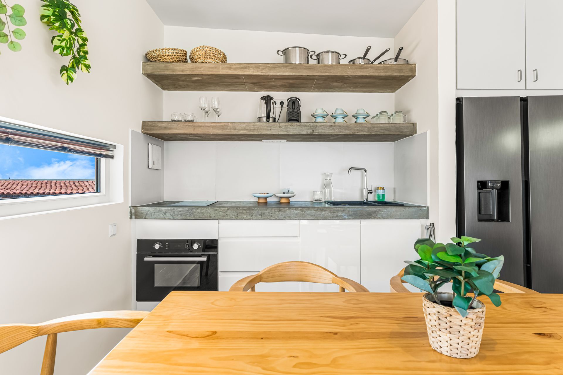 Modern kitchen with wooden table, open shelves, white cabinets, and stainless steel refrigerator