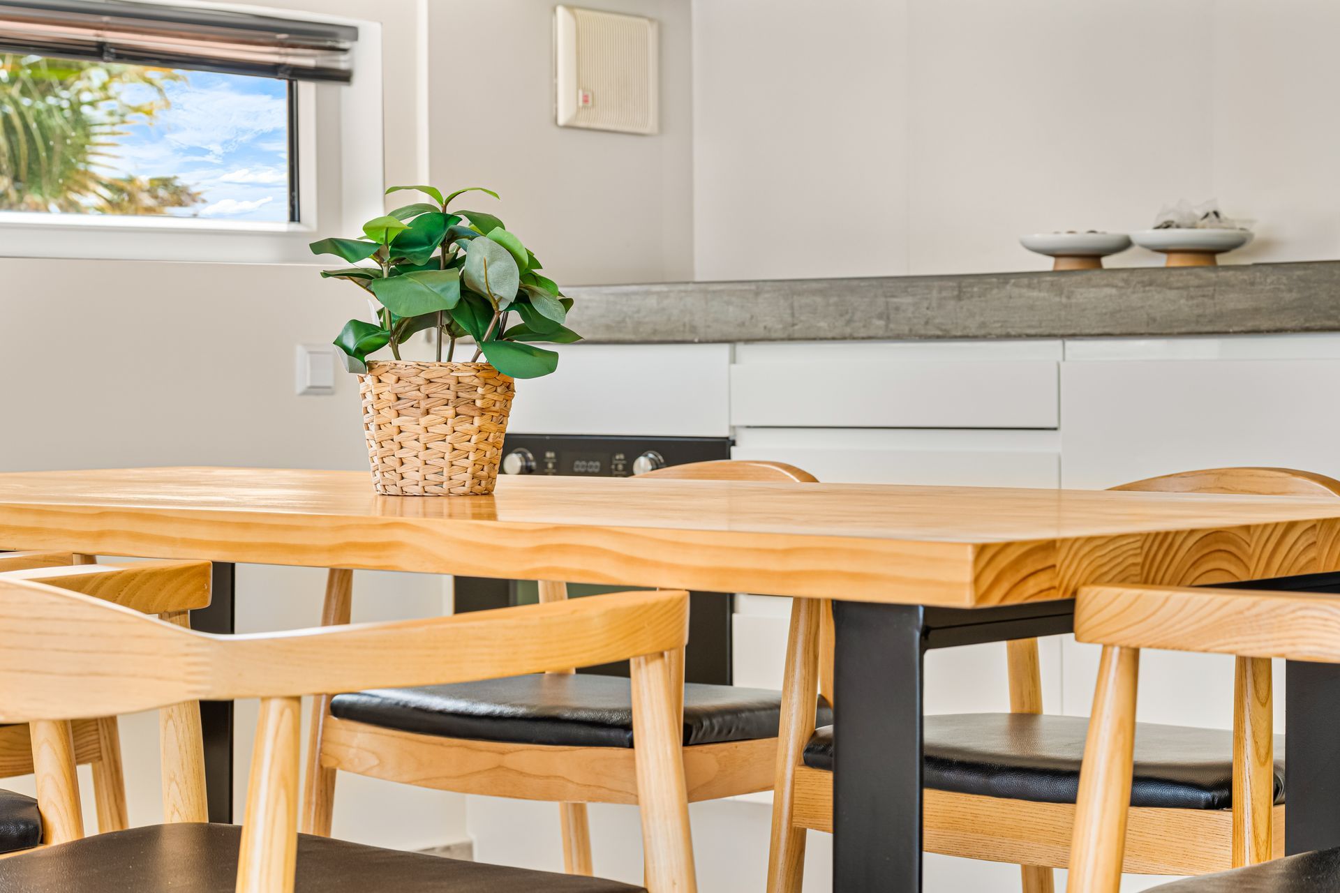 Bright dining room with wooden table, matching chairs, and a potted plant by a window