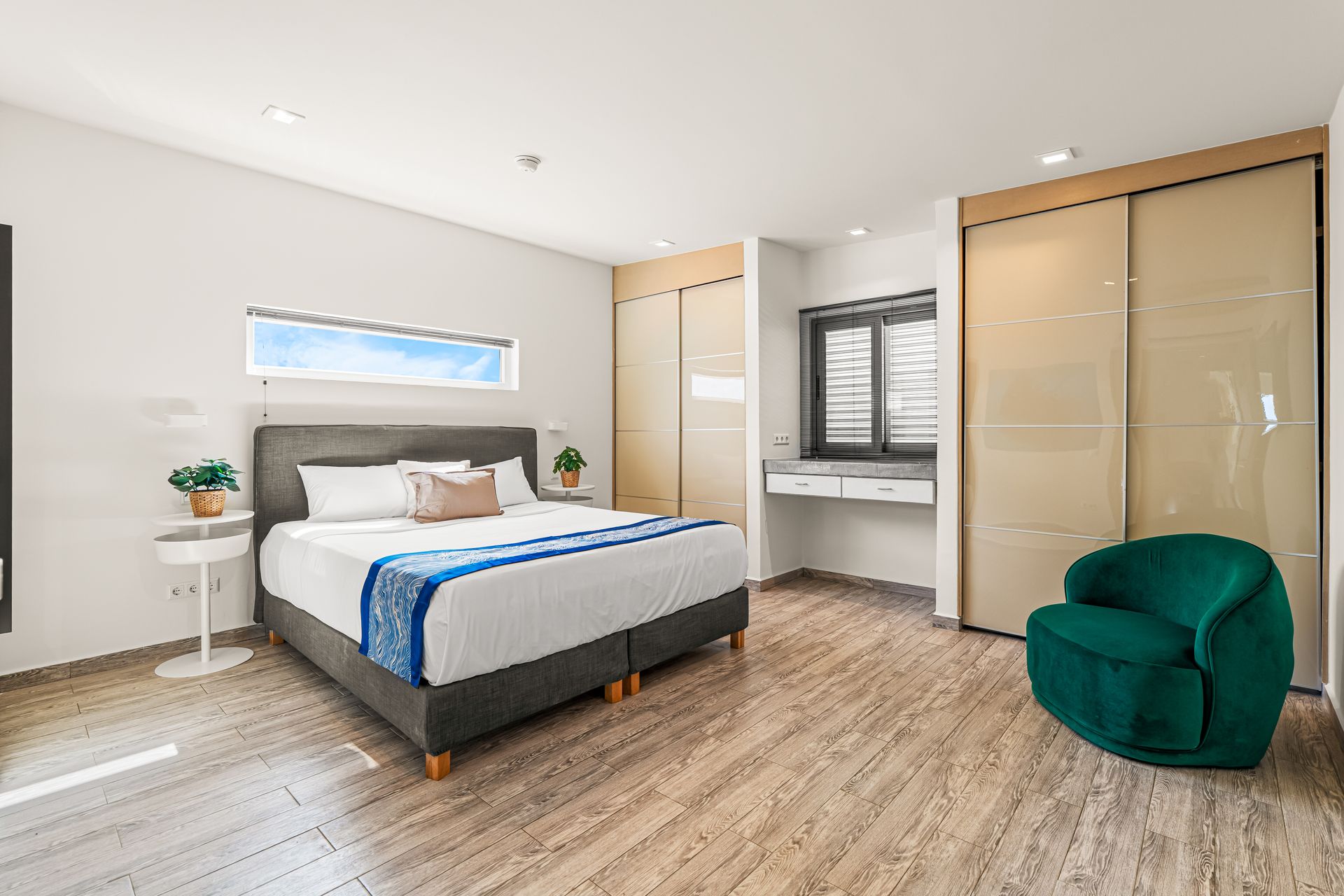 Bright modern bedroom with a bed, desk nook, beige wardrobe, and green chair on wood flooring.