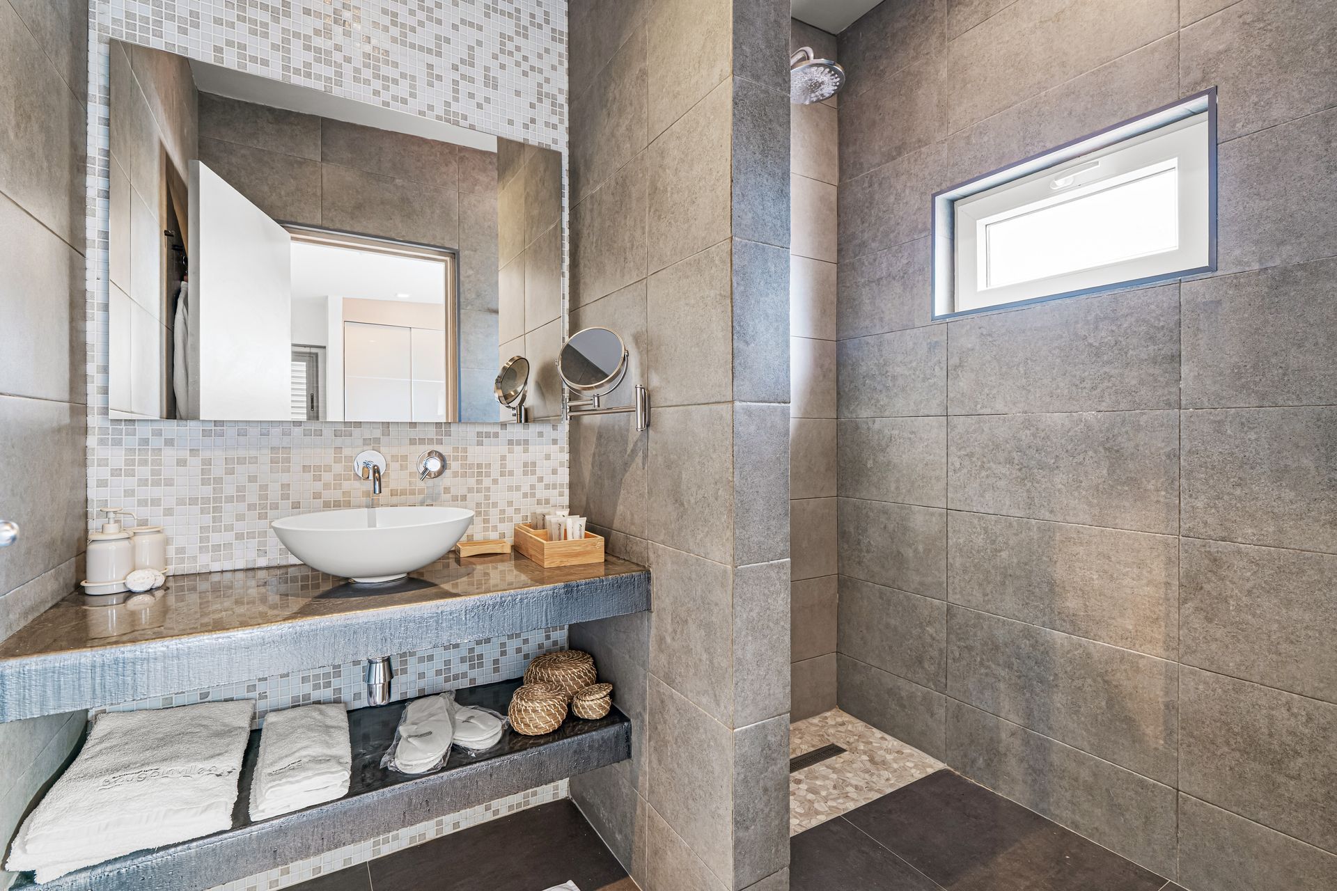 Modern bathroom with stone vanity, wall mirror, vessel sink, and walk-in shower with small window