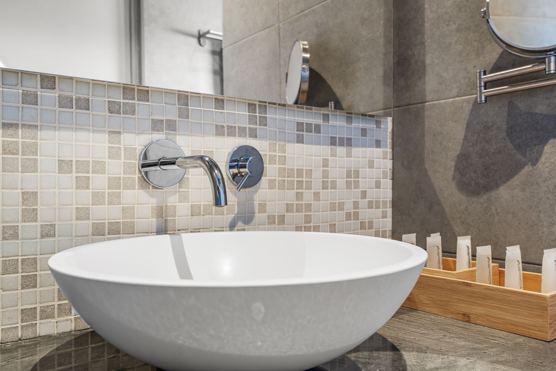 Modern bathroom sink with a white vessel basin, chrome faucet, mosaic tile backsplash, and toiletry tray.