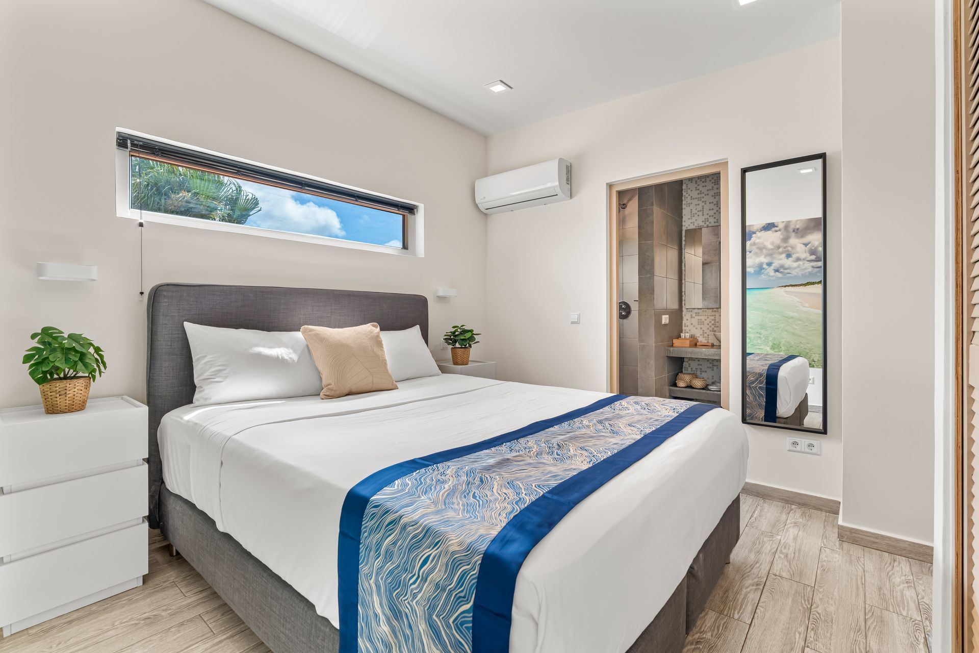 Bright modern bedroom with a bed, blue runner, white dresser, mirror, and wall-mounted air conditioner