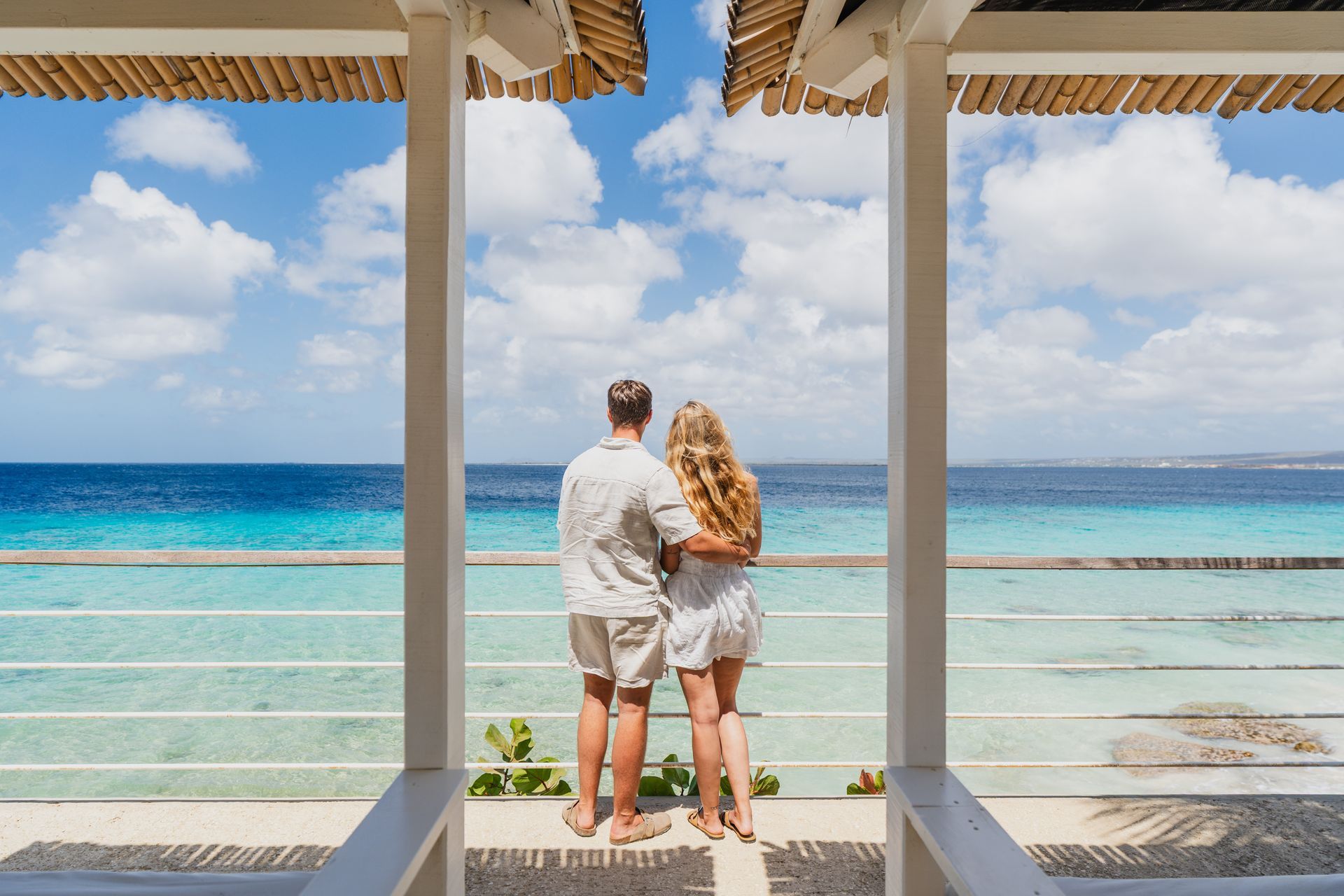 Couple standing on a balcony overlooking a turquoise ocean and blue sky