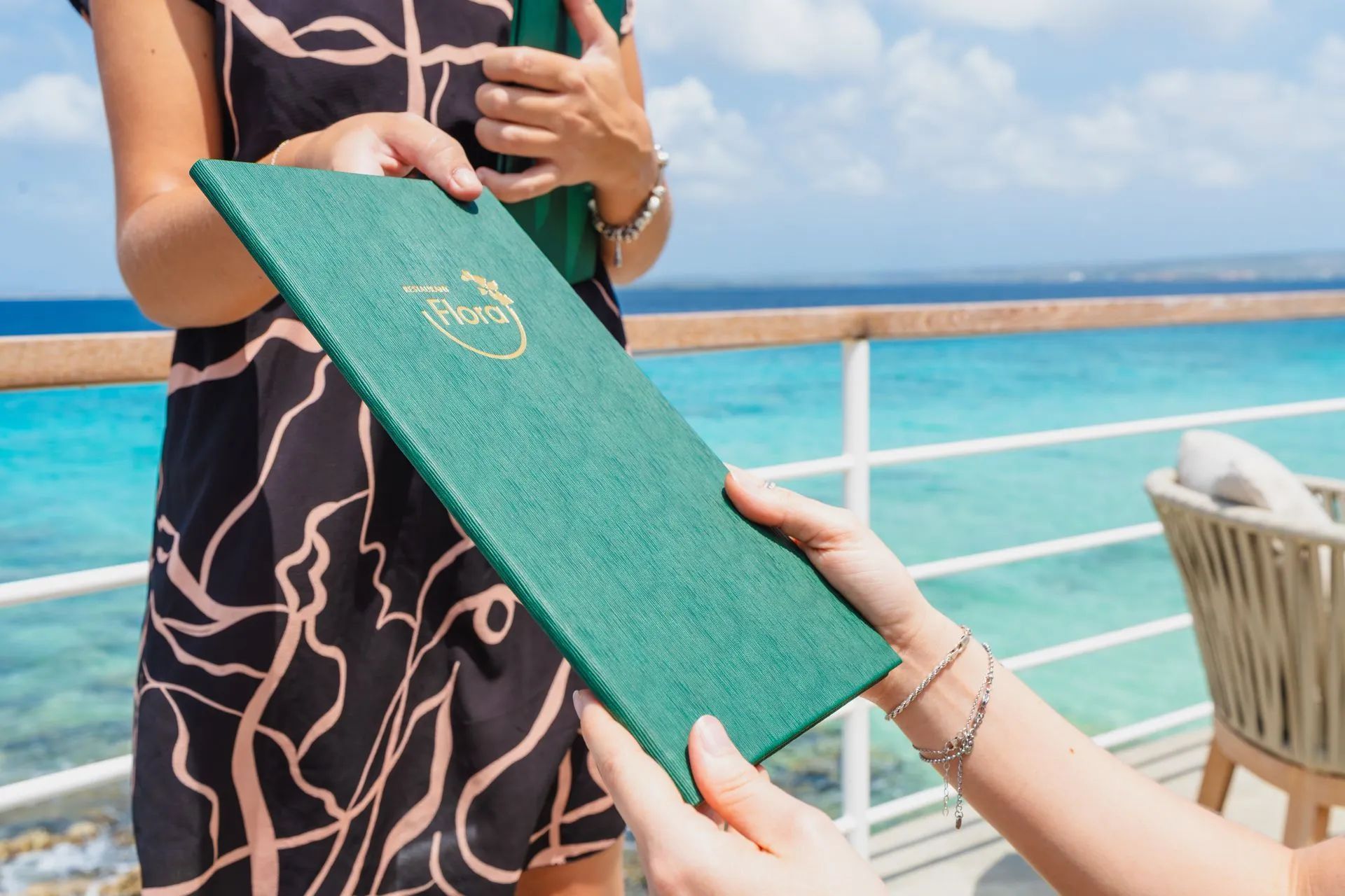 Two people holding a green menu on a deck overlooking the blue ocean.