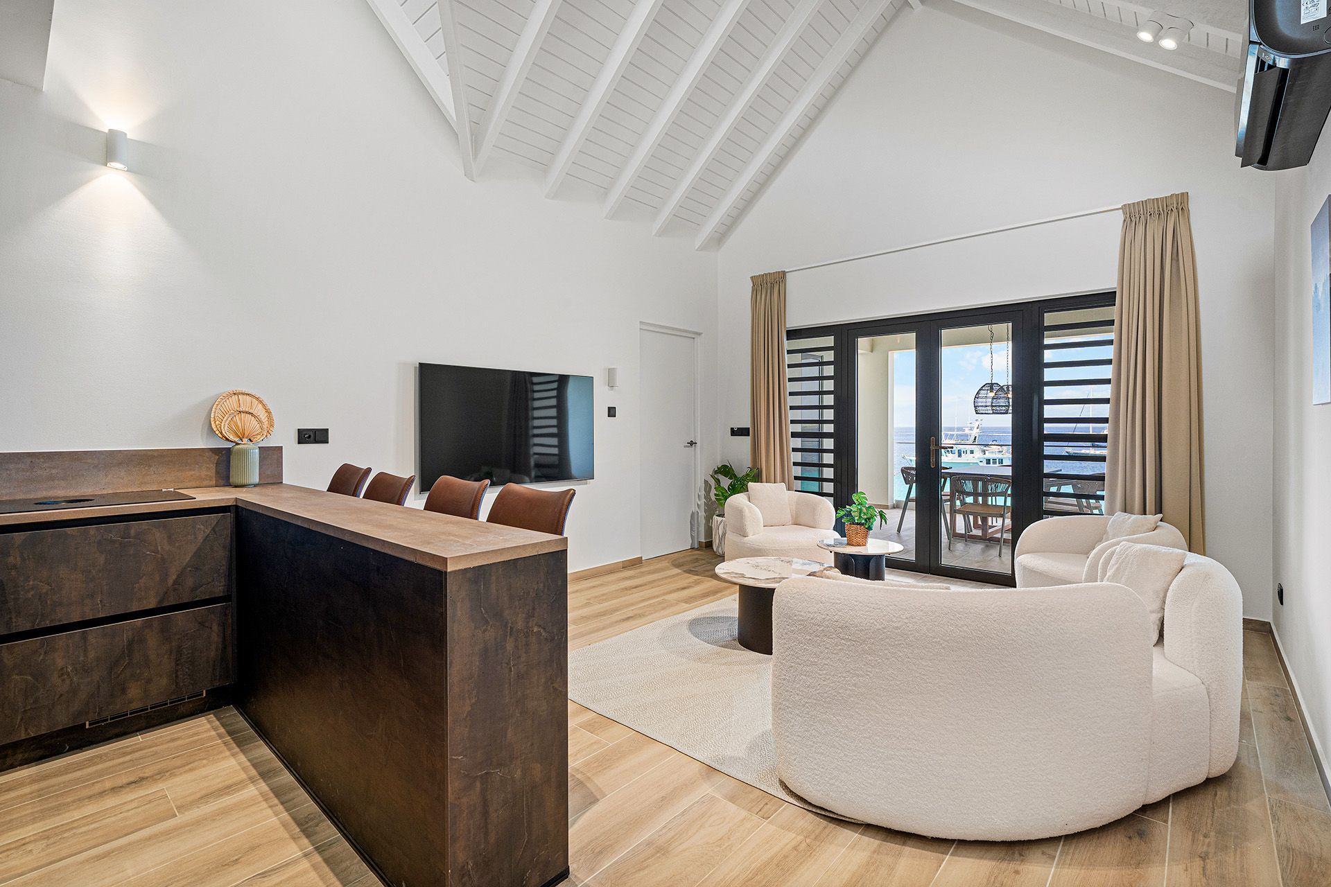 Modern living room with kitchen, two cream armchairs, and deck access.