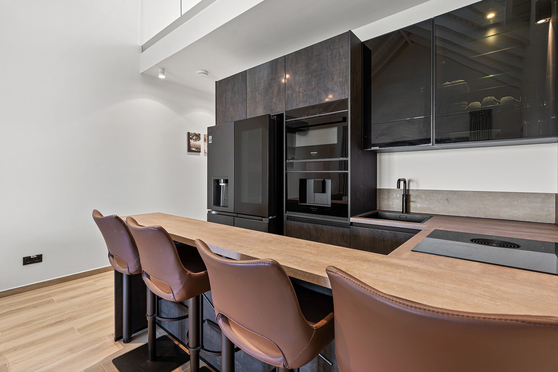 Modern kitchen with brown leather bar stools, dark cabinetry, and a wooden counter.
