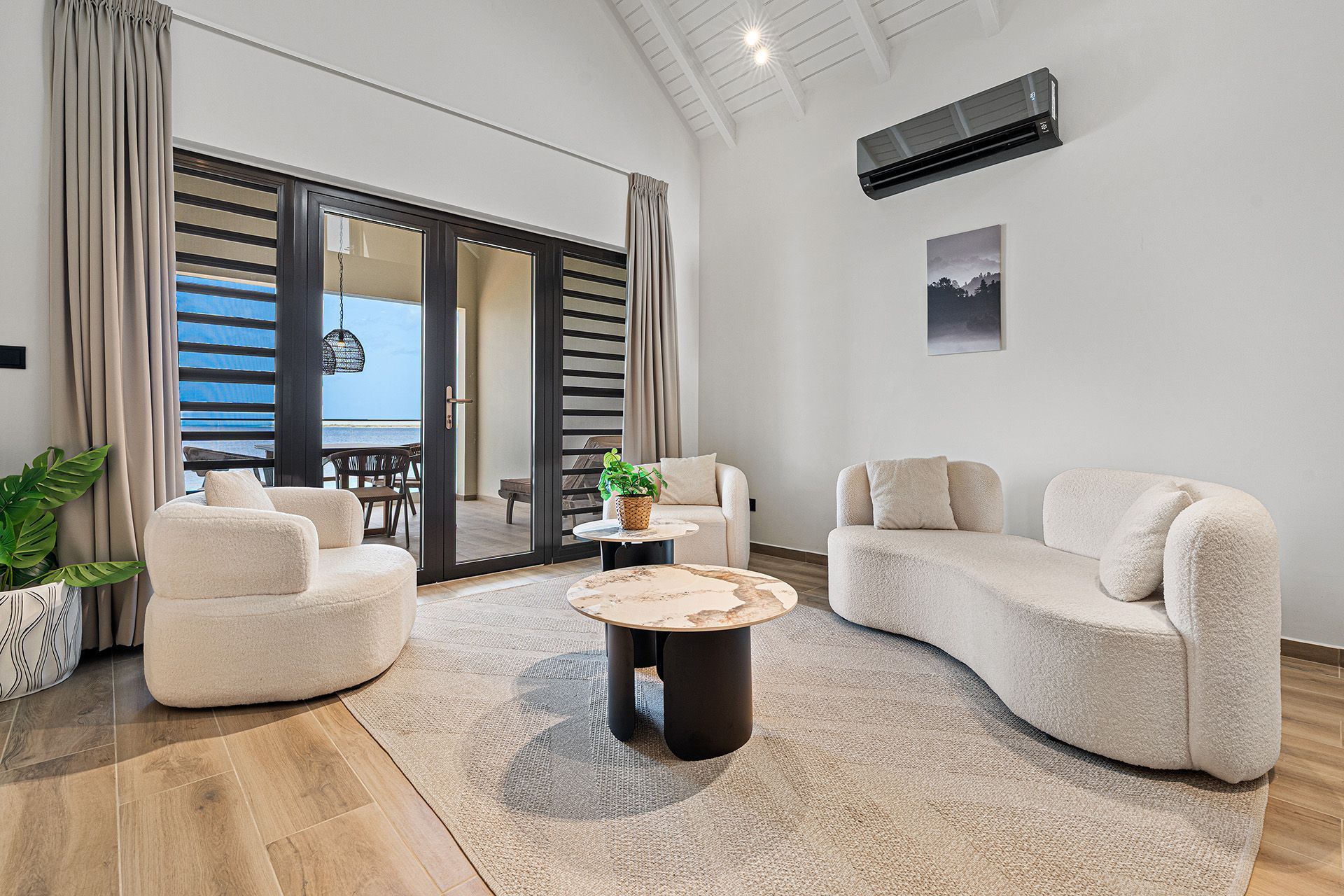 A modern living room with beige furniture, a rug, and a sliding door leading to an outdoor dining area.