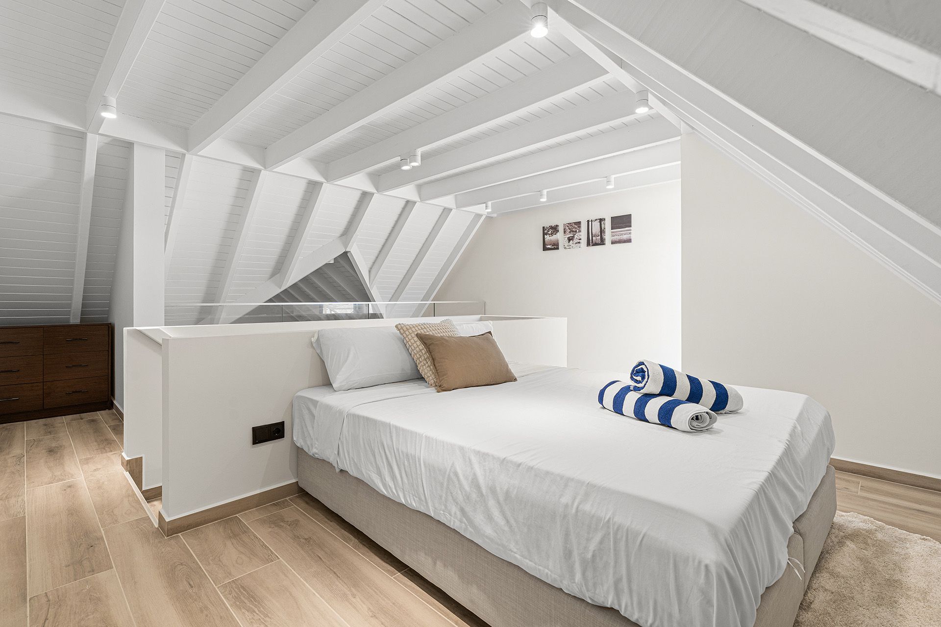 Bedroom with a bed, white walls, angled ceiling, and wood floor.