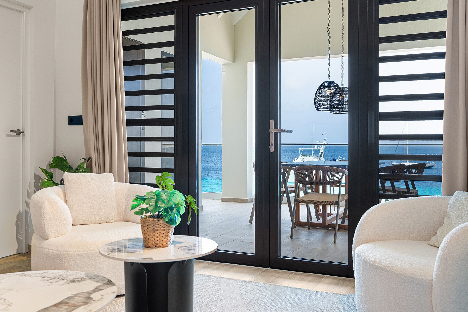 Living room with ocean view: white chairs, round table, open glass doors to balcony with seating.