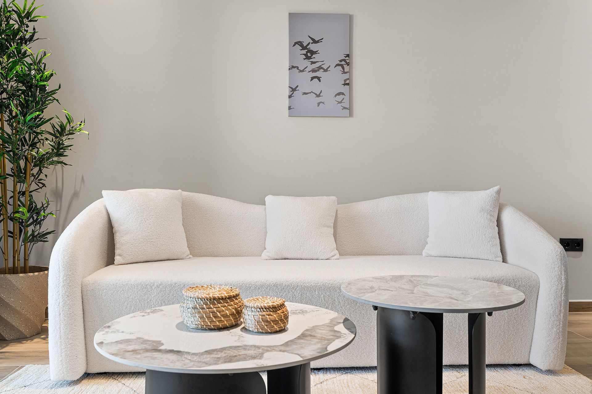 White couch with pillows and two marble-topped coffee tables in a neutral living room.