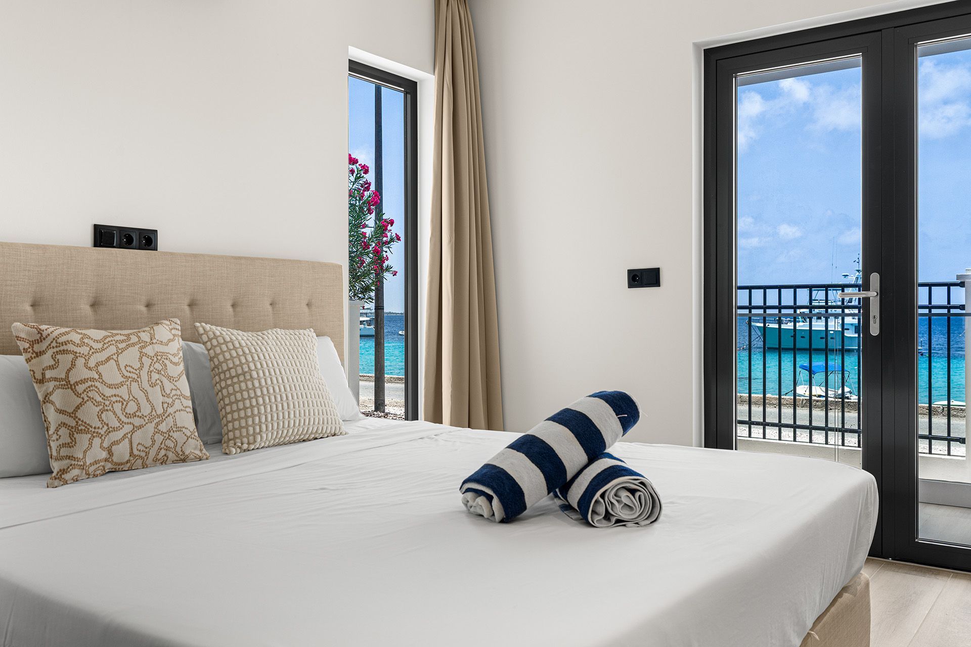 Bedroom with white bed, open door to balcony with ocean view, rolled towels.