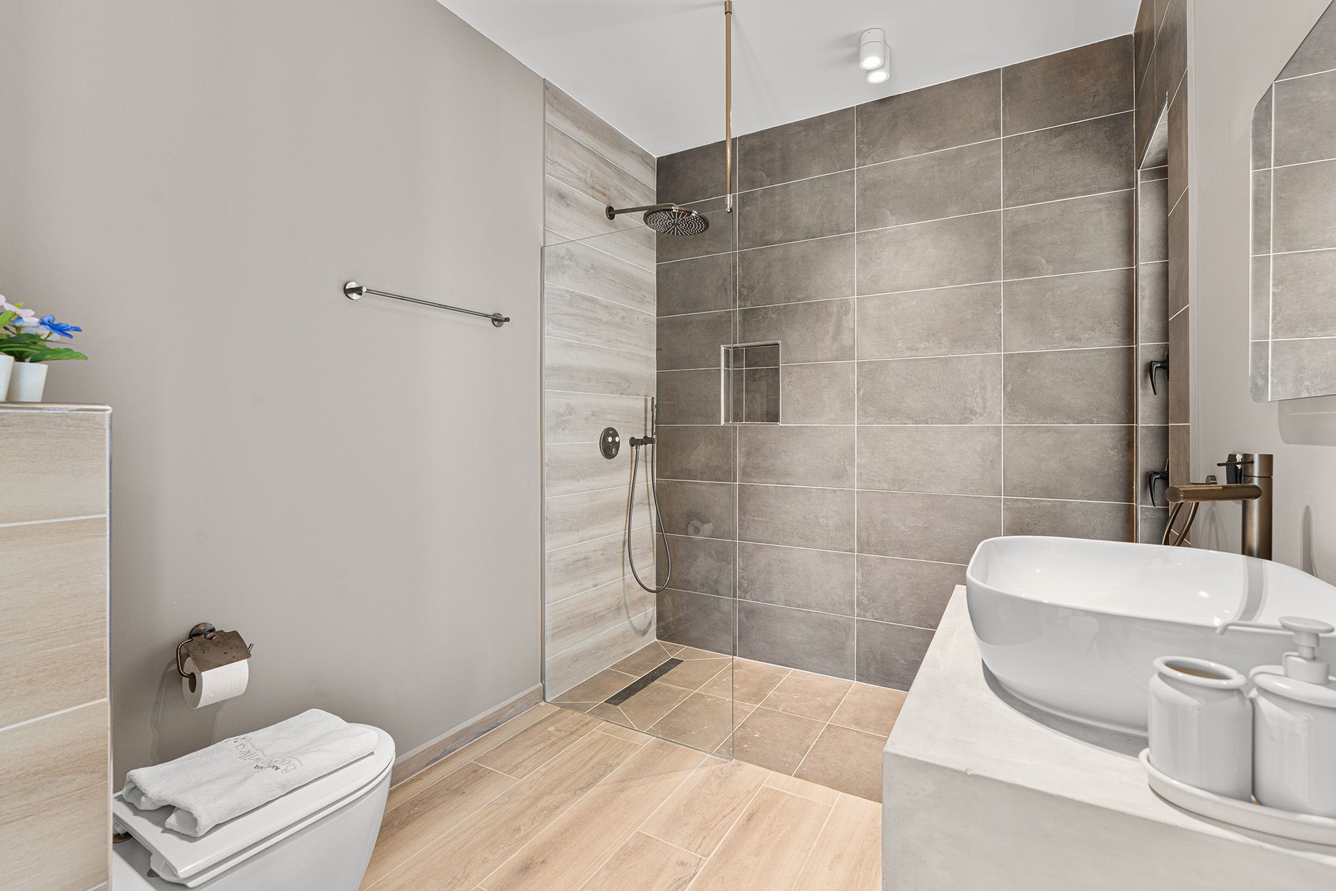 Modern bathroom with a walk-in shower, floating sink, toilet, and gray tile walls and floors.