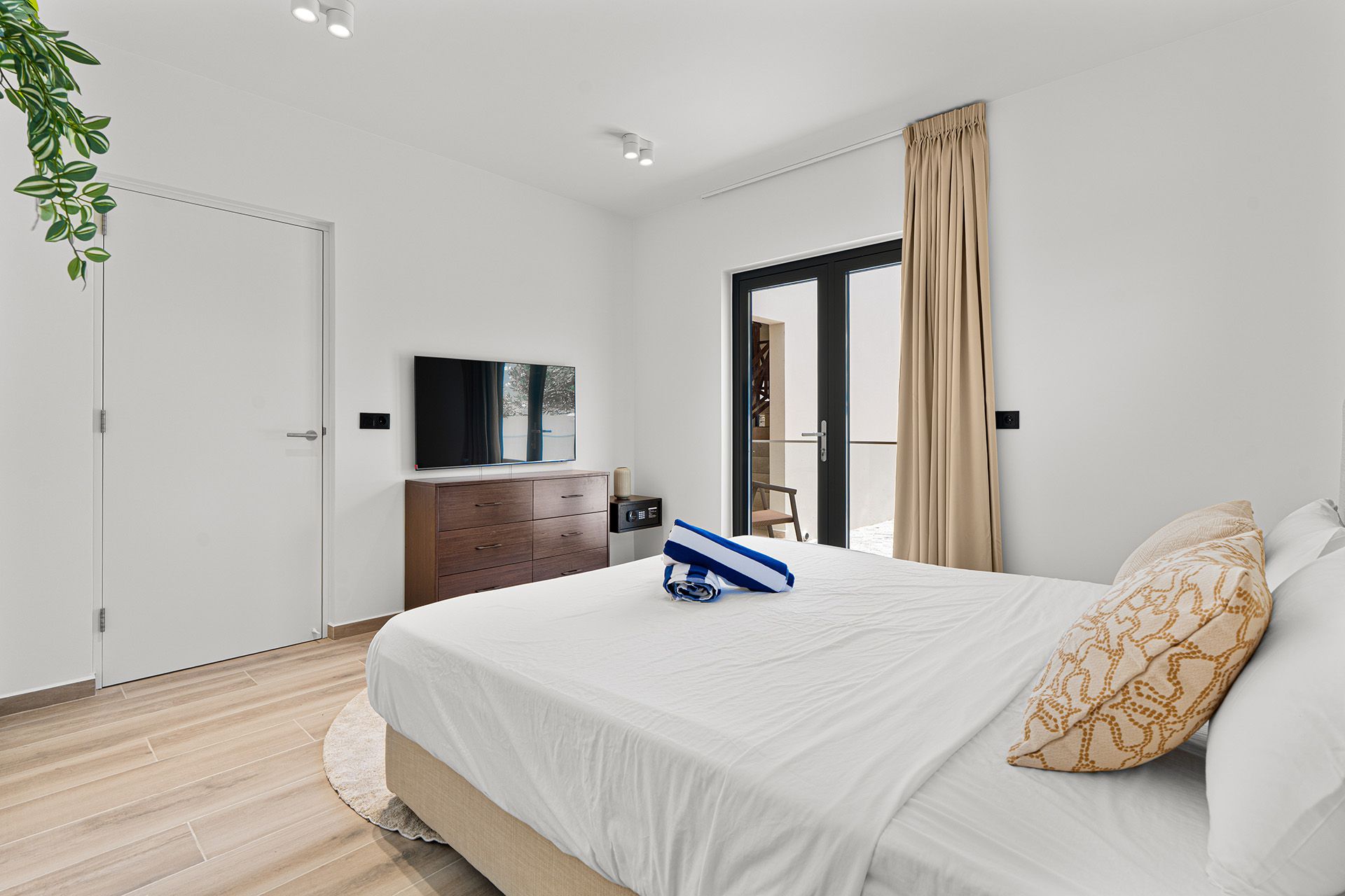 Bedroom with white walls, bed, dresser, TV, and door to a balcony.