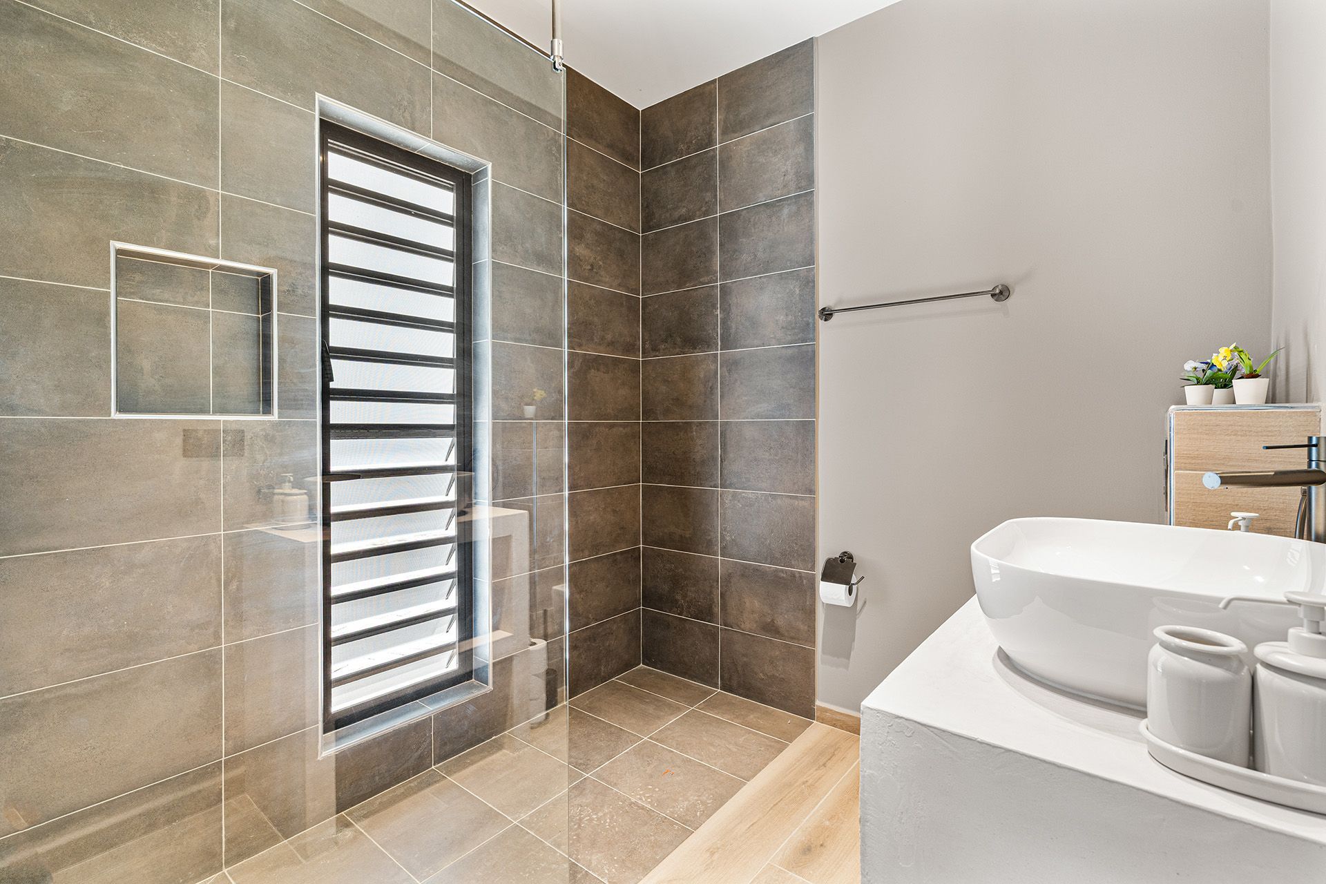 Modern bathroom with tiled walls, window with blinds, and a vessel sink on a white countertop.