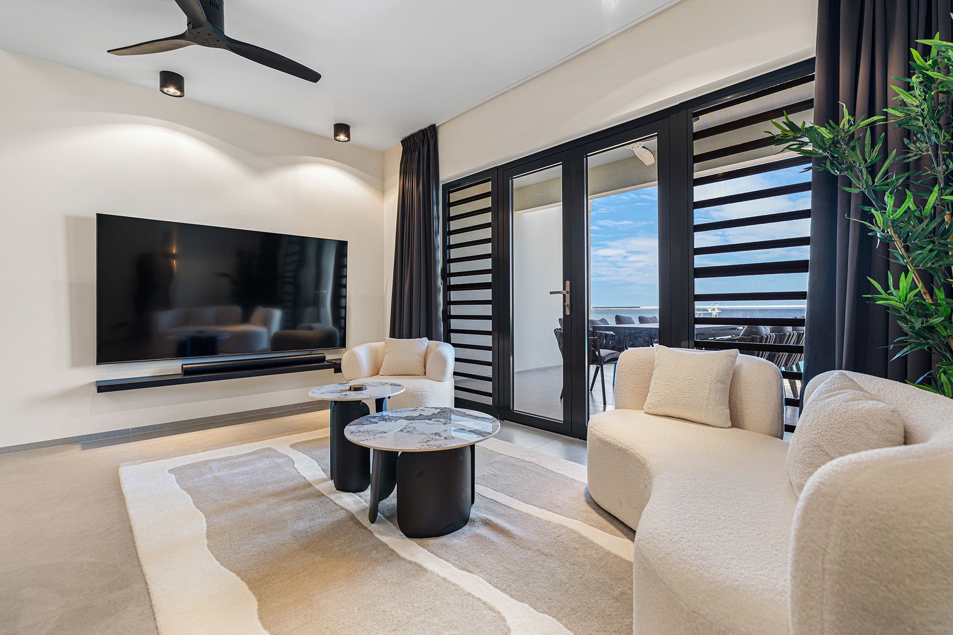 Living room with black TV, white chairs, and glass doors to a balcony.