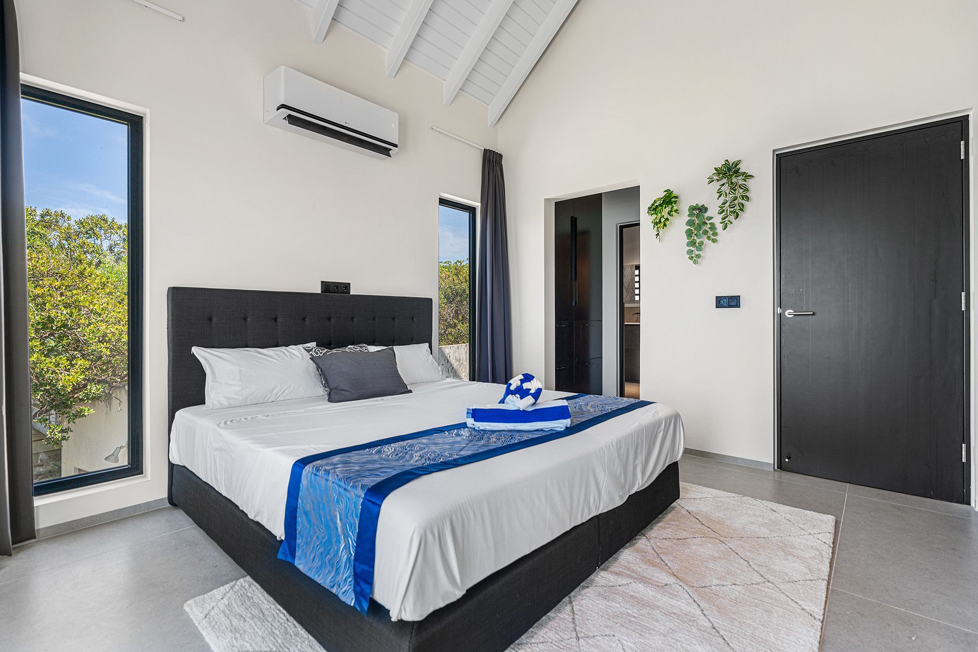 Bedroom with a large bed, dark headboard, blue accents, large window, black door.