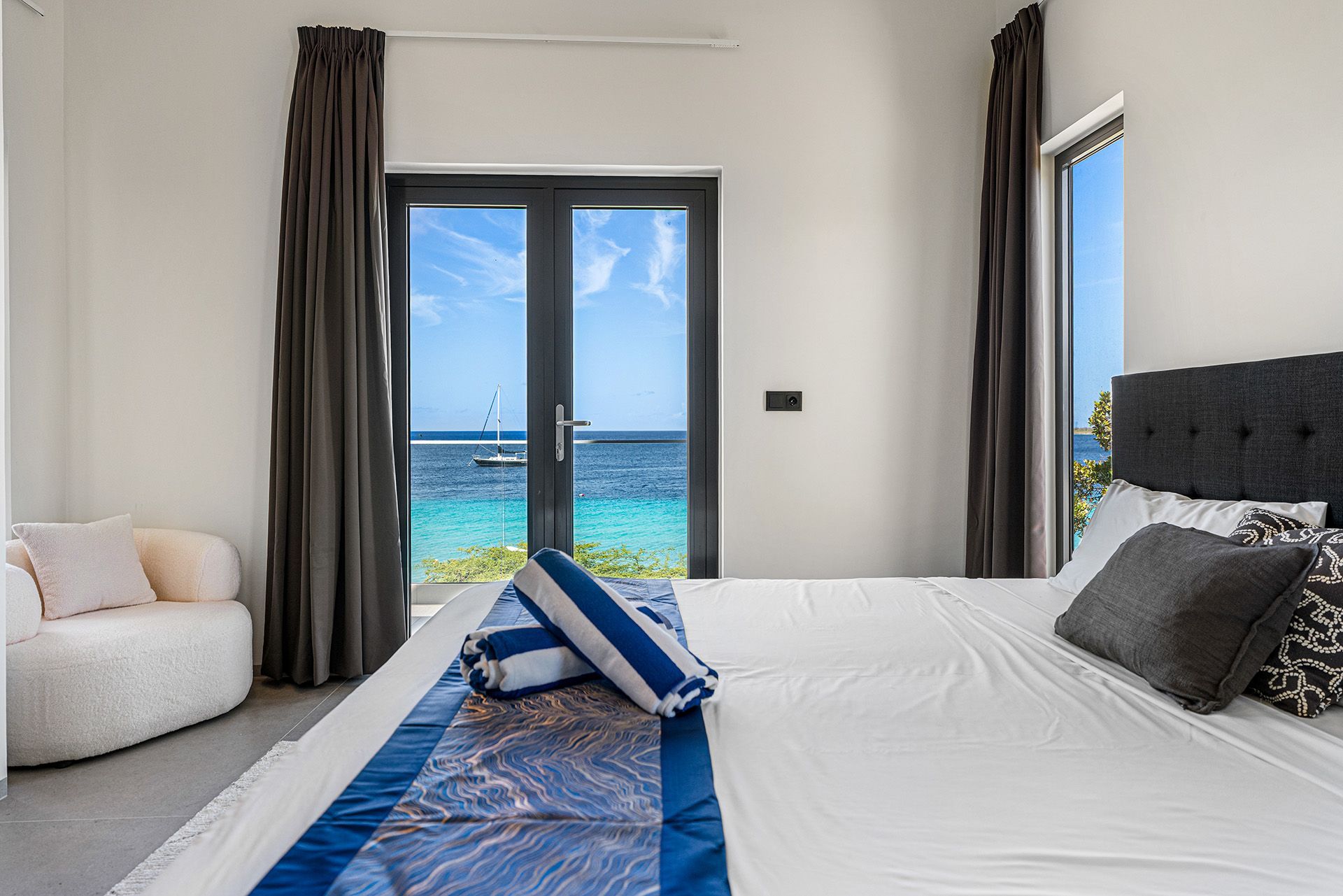 Bedroom with bed, ocean view through doors, gray and white decor.