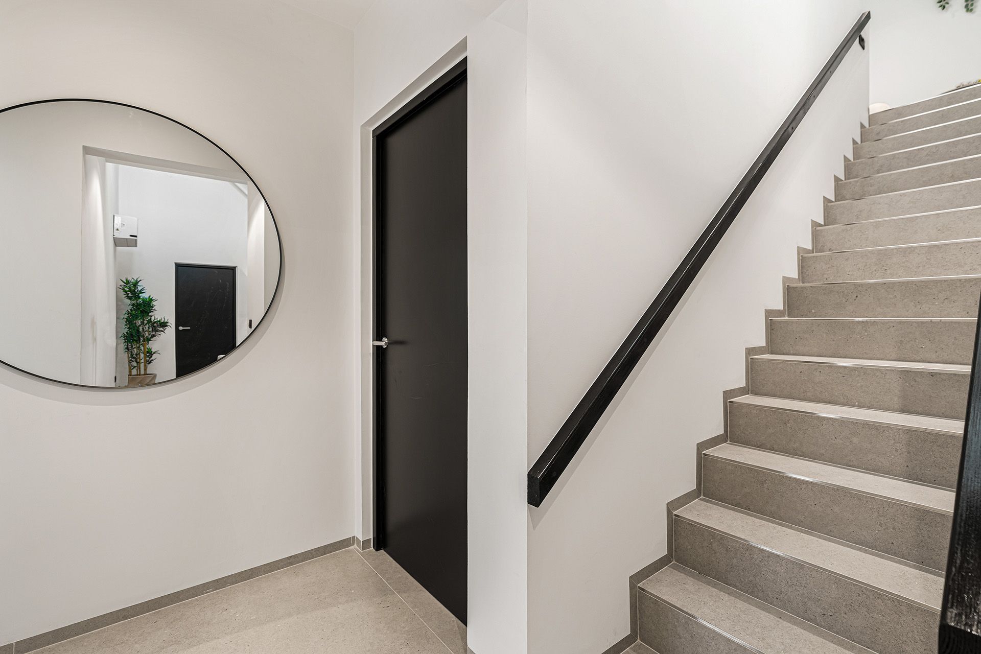 Hallway with stairs and a round mirror. A black door is next to the stairs.