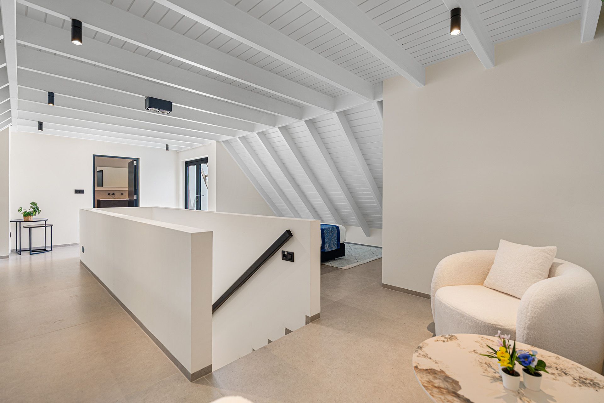 Bright, modern interior with white walls, exposed beams, a seating area, and a staircase.