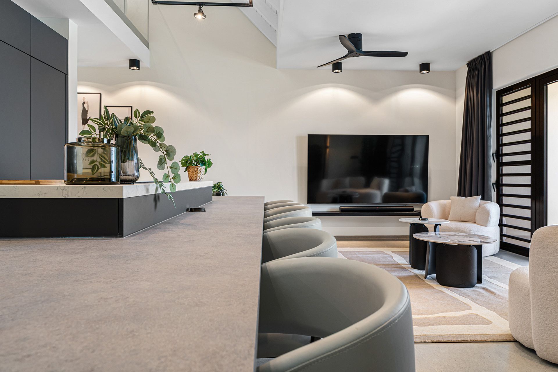 Modern living room with TV, gray sofa, and chairs. Neutral color palette with plants.