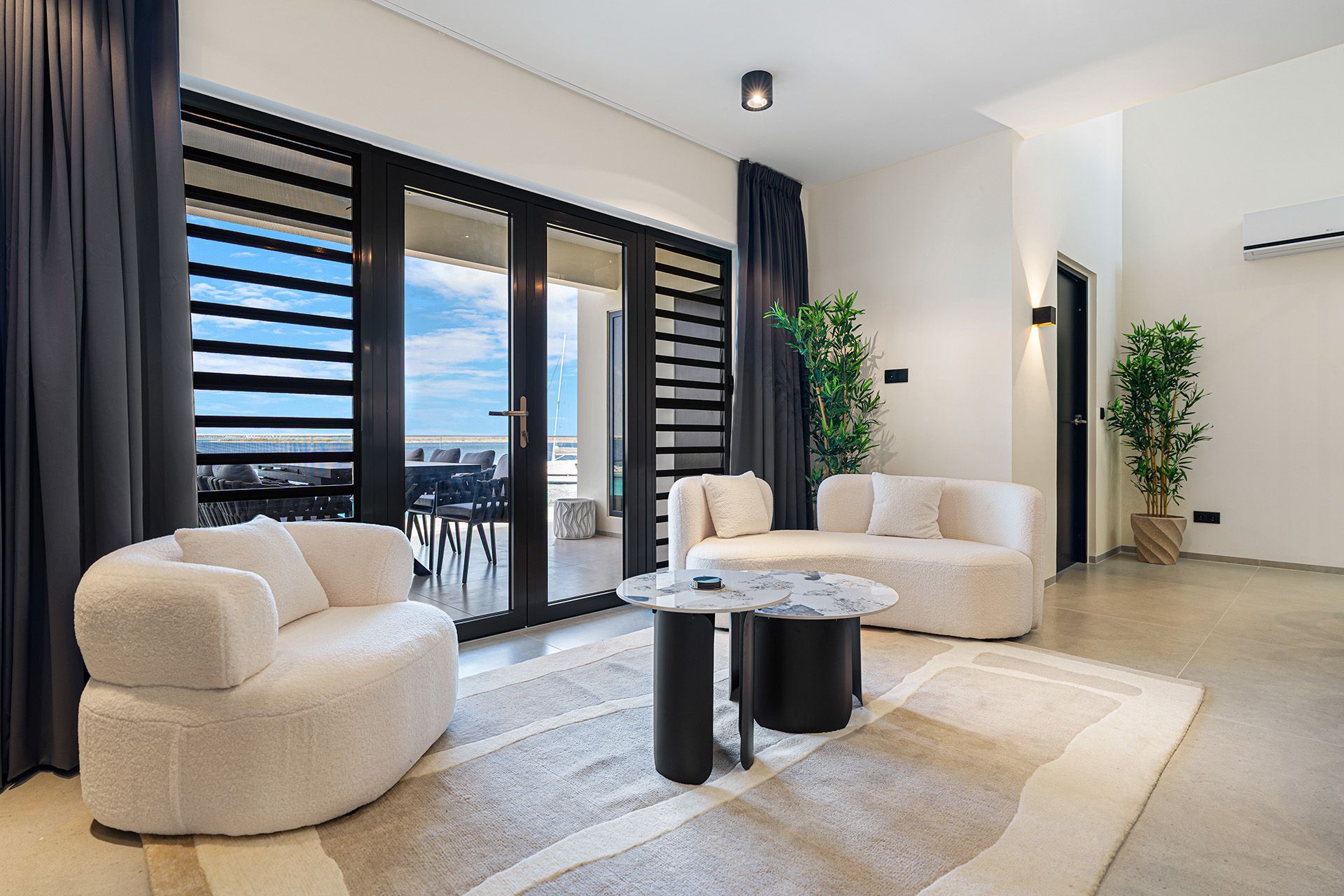 Living room with white sofa, arm chair, dark drapes, and a view of a deck and the ocean.