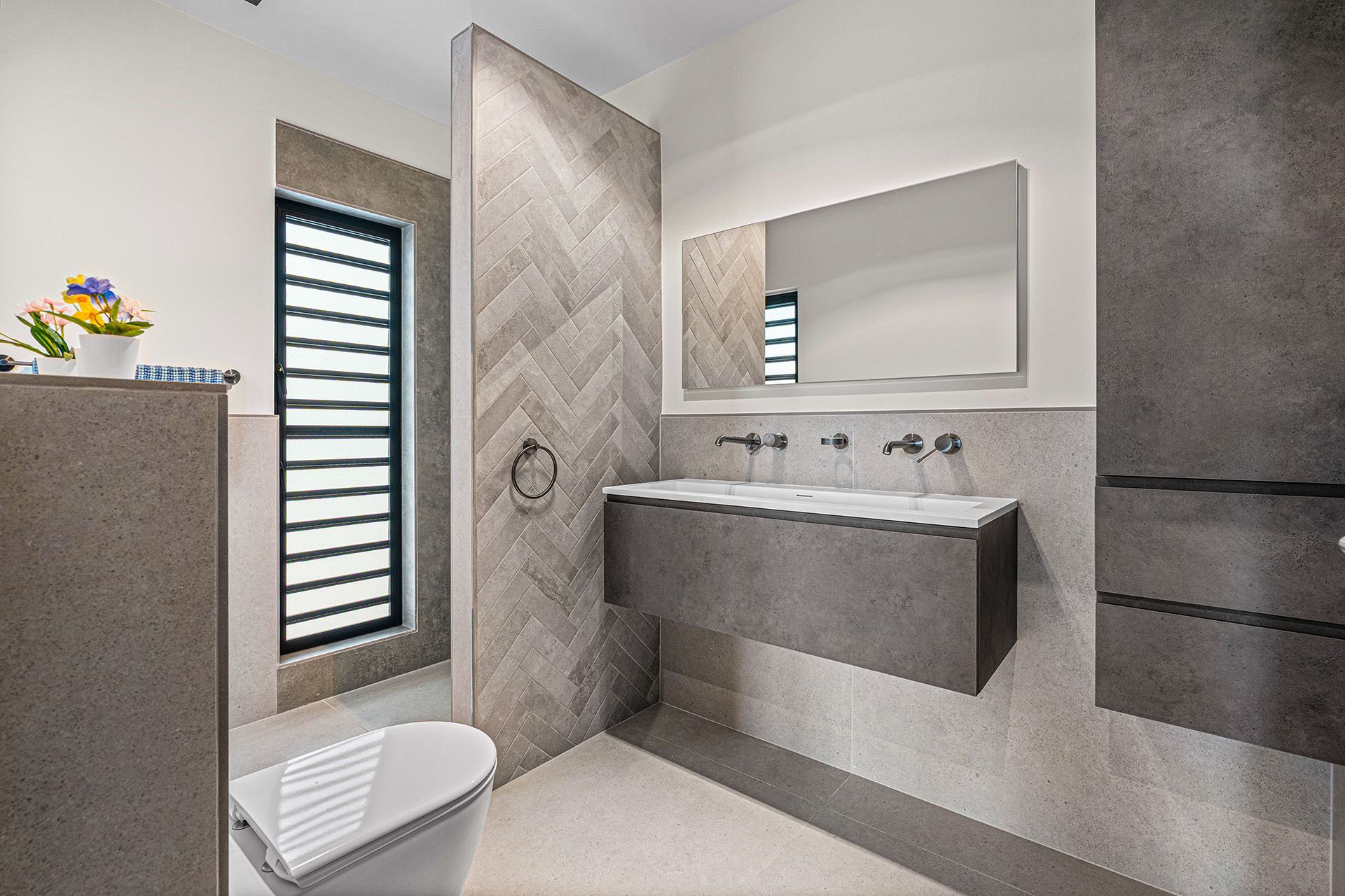 Modern bathroom with gray tiles, floating vanity, large mirror, and a window.