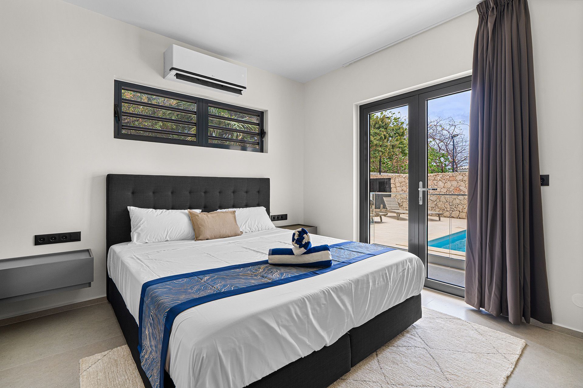 Bedroom with a bed, sliding door to a pool, air conditioner, and dark gray curtains.