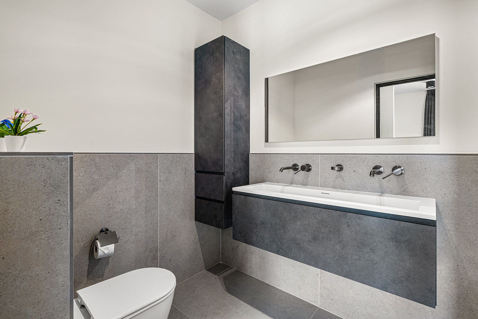 Modern bathroom with gray concrete walls, floating vanity, and tall storage cabinet.