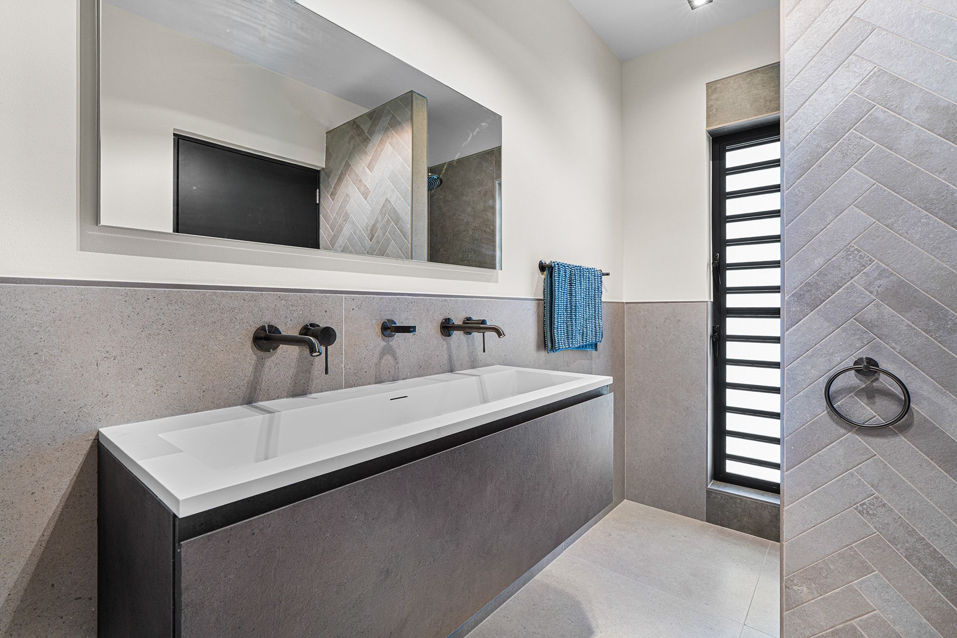 Modern bathroom with gray and white color scheme. Floating double sink, large mirror, herringbone tile accent wall.