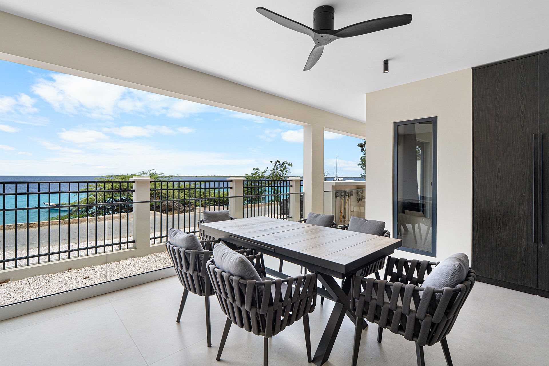 Patio with dining table and chairs, ocean view, blue sky, and a ceiling fan.