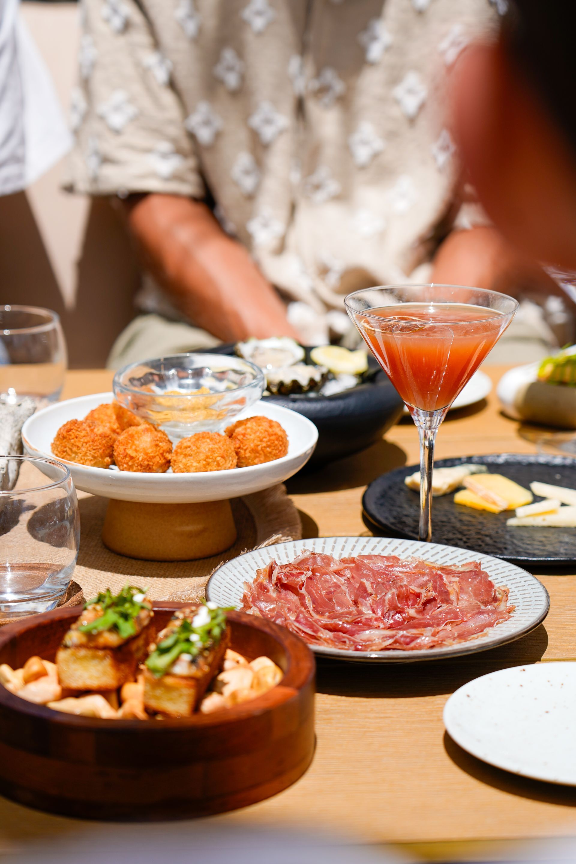 Japanese-style shared meal with sushi, tempura, sliced beef, and cocktails on a wooden dining table