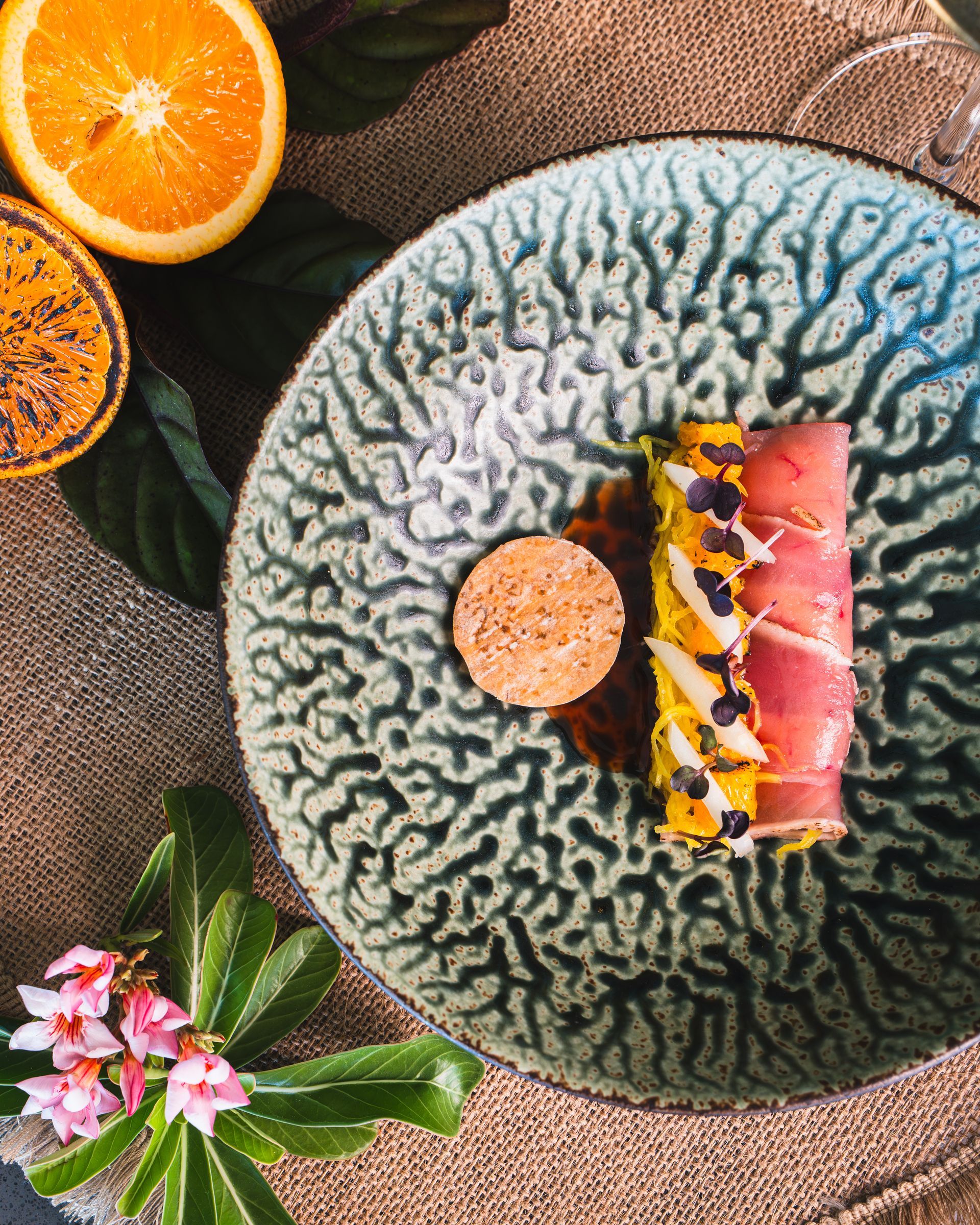 Gourmet dish on patterned teal plate, featuring wrapped meat, a circular cracker, and orange slices.