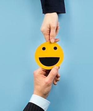 Two hands holding a yellow smiley face in the middle against a blue background to represent our commitment to customer satisfaction.