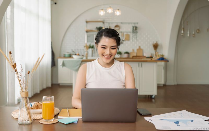 Woman at home smiling while looking at her laptop.