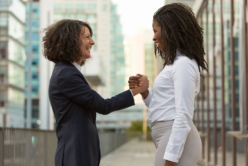 Two people holding hands after a success and smiling at each other.