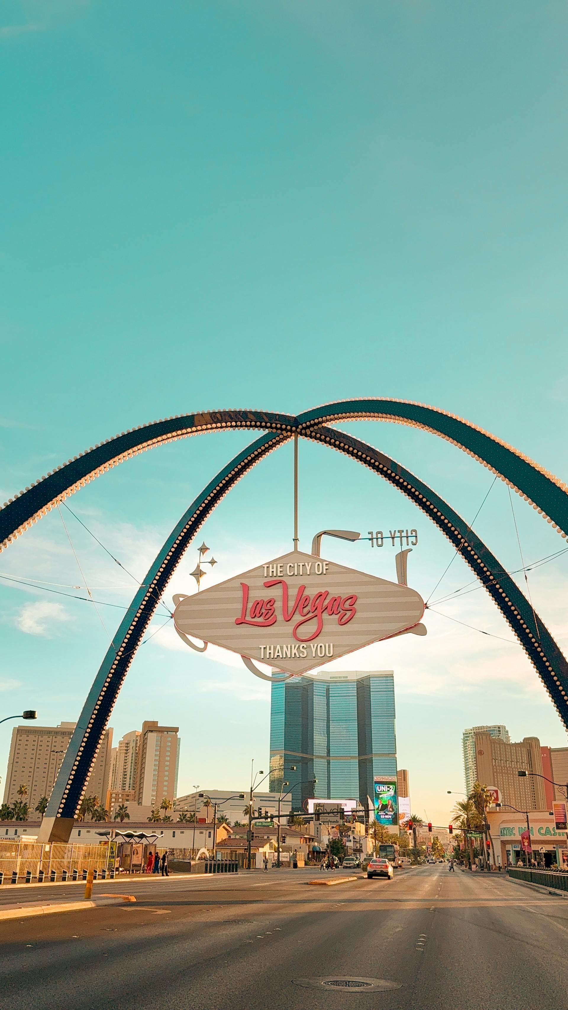 Las Vegas welcome sign with arch against a clear, blue sky. City buildings line the street.