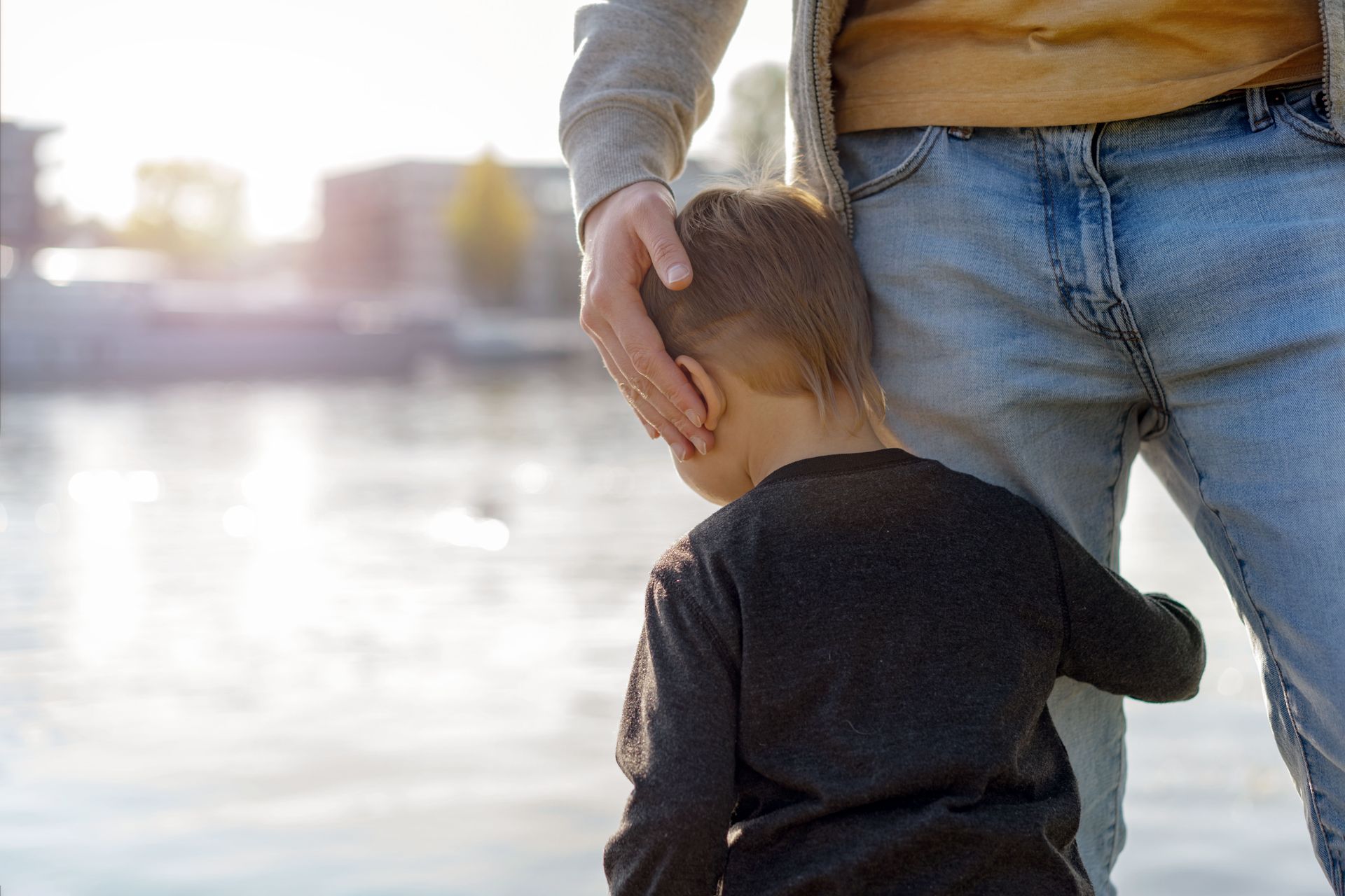 Adult holding a child’s head by the water at sunset