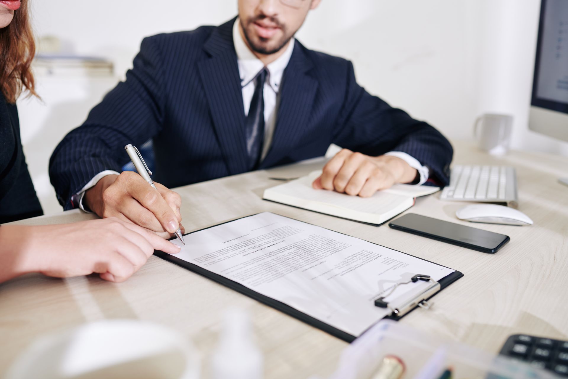 Two people signing a document at a desk in a business meeting
