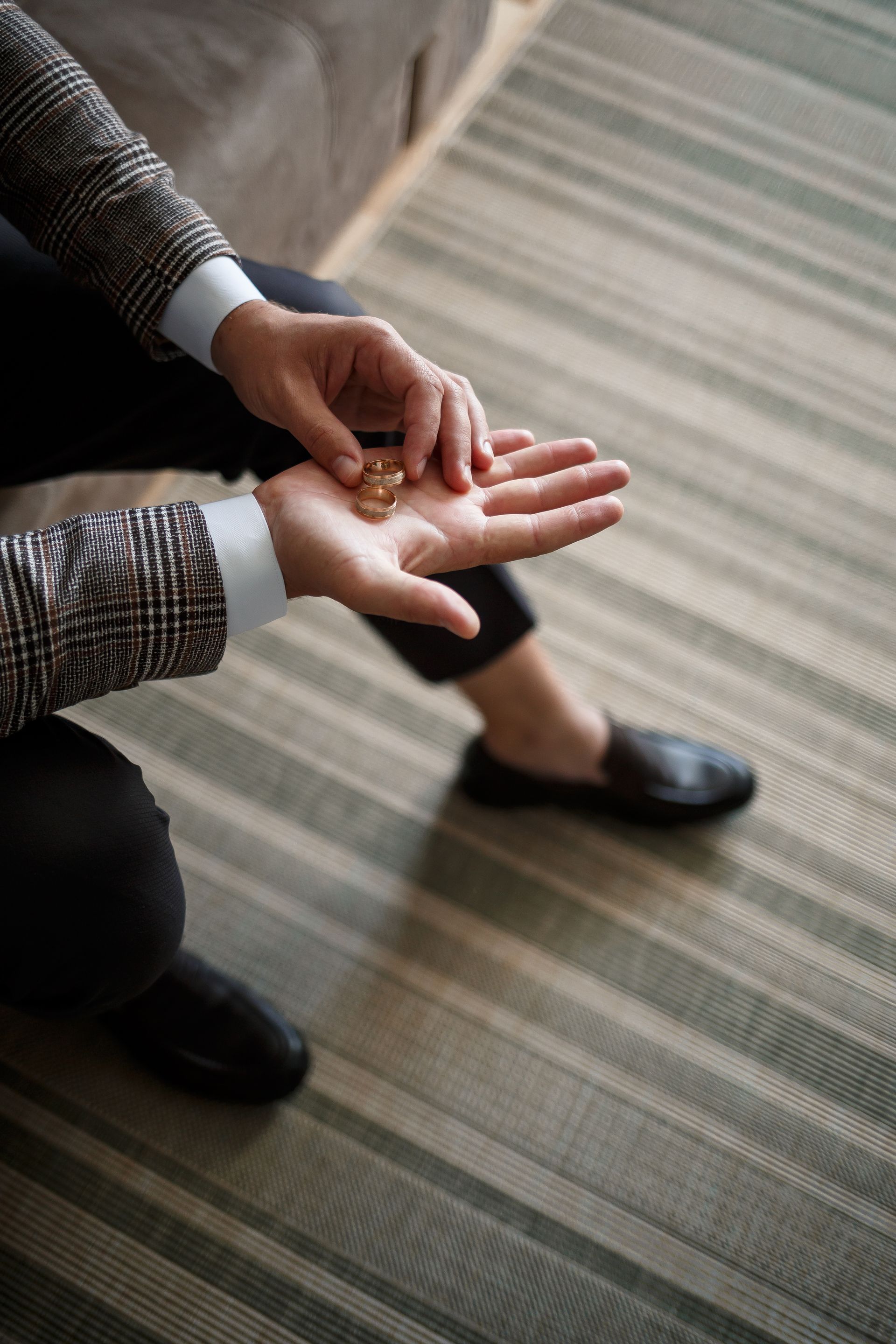 Person rubbing a hand with the other hand while sitting on a striped carpet indoors