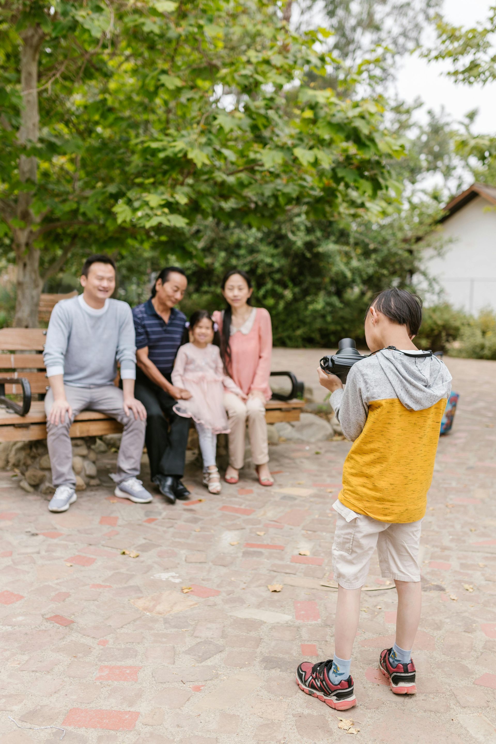 Boy photographing family sitting on bench in park.
