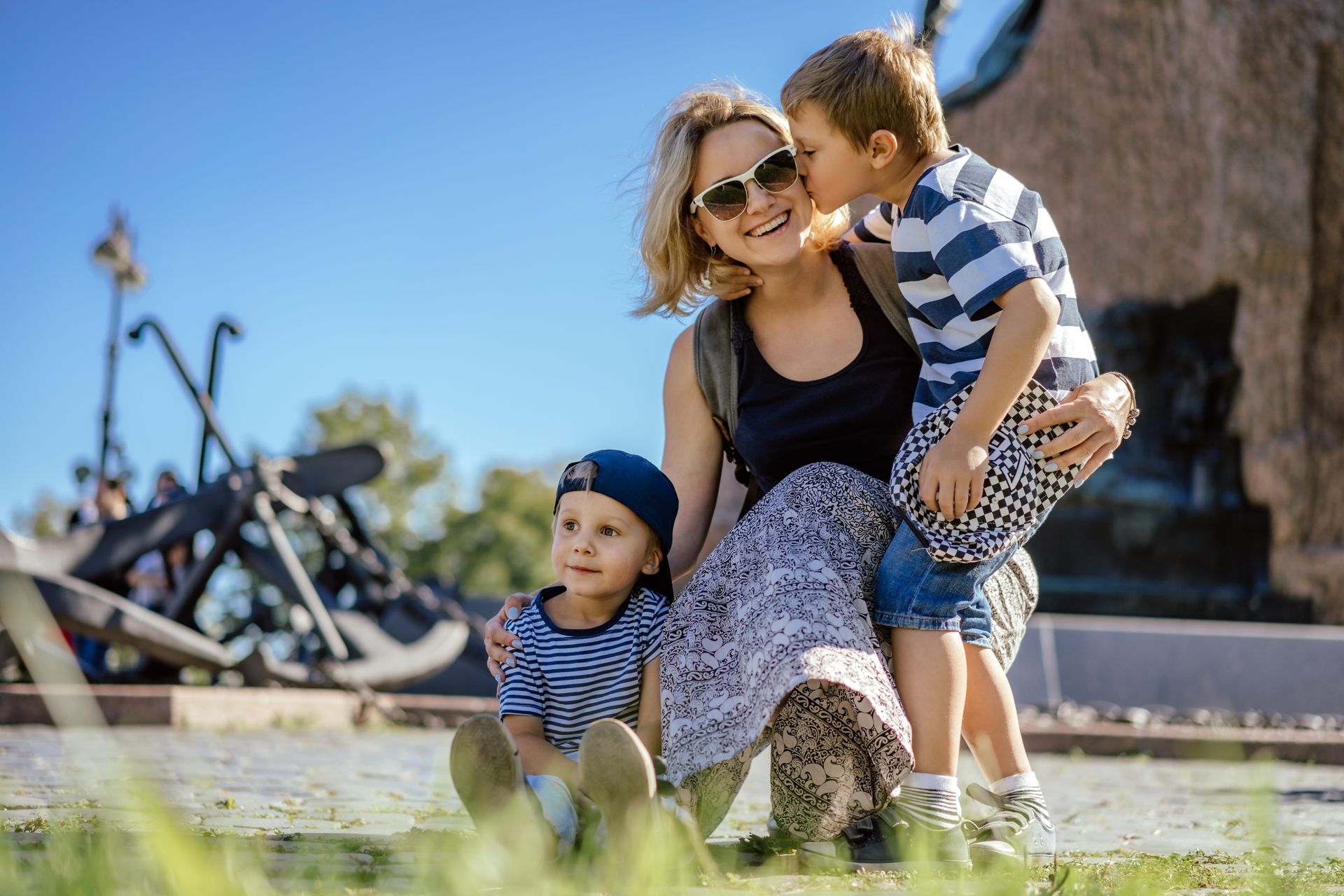 Woman and two children sitting on grass outdoors, smiling near a building and bicycles.