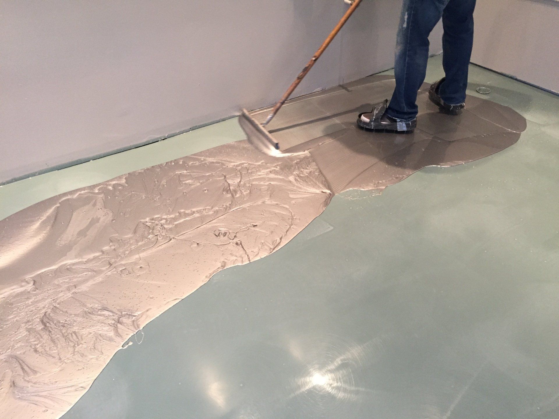 Person spreading beige coating on a glossy green floor with a trowel during floor installation.