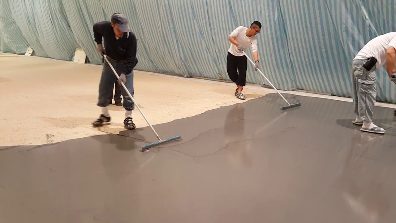 Three workers smoothing wet concrete with long-handled squeegees on a construction site.