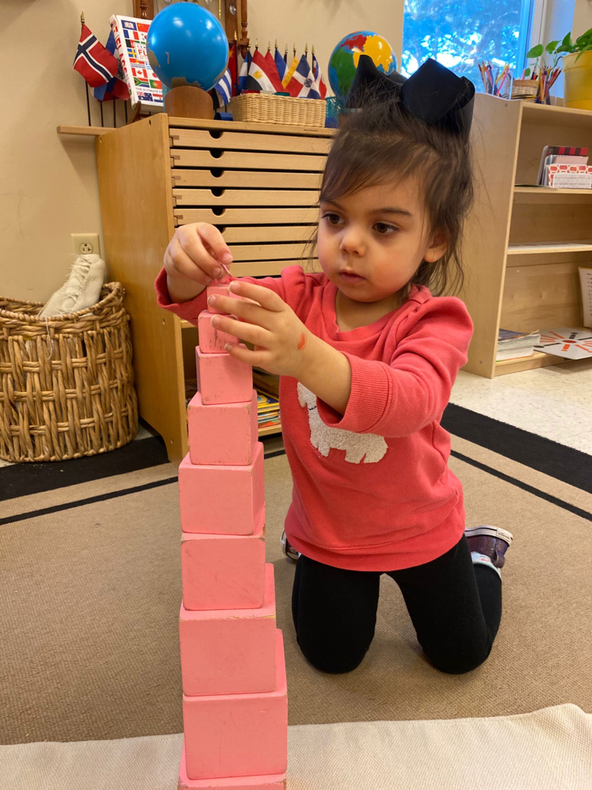 a Montessori child is kneeling on the floor playing with pink blocks