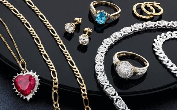 A gold chain with a heart pendant, two rings, a bracelet, and various earrings arranged on a black surface.
