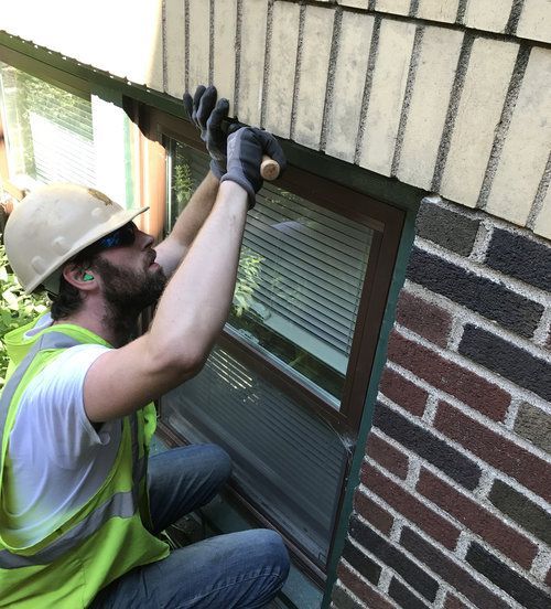 A man wearing a hard hat and safety vest is working on a brick wall