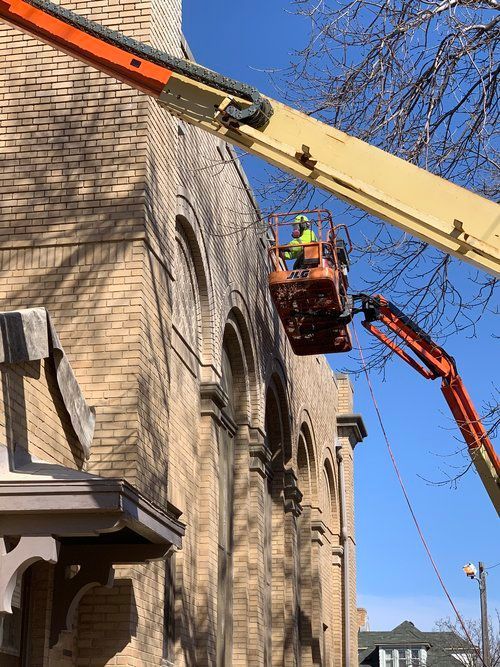 A man is working on a crane on the side of a brick building.